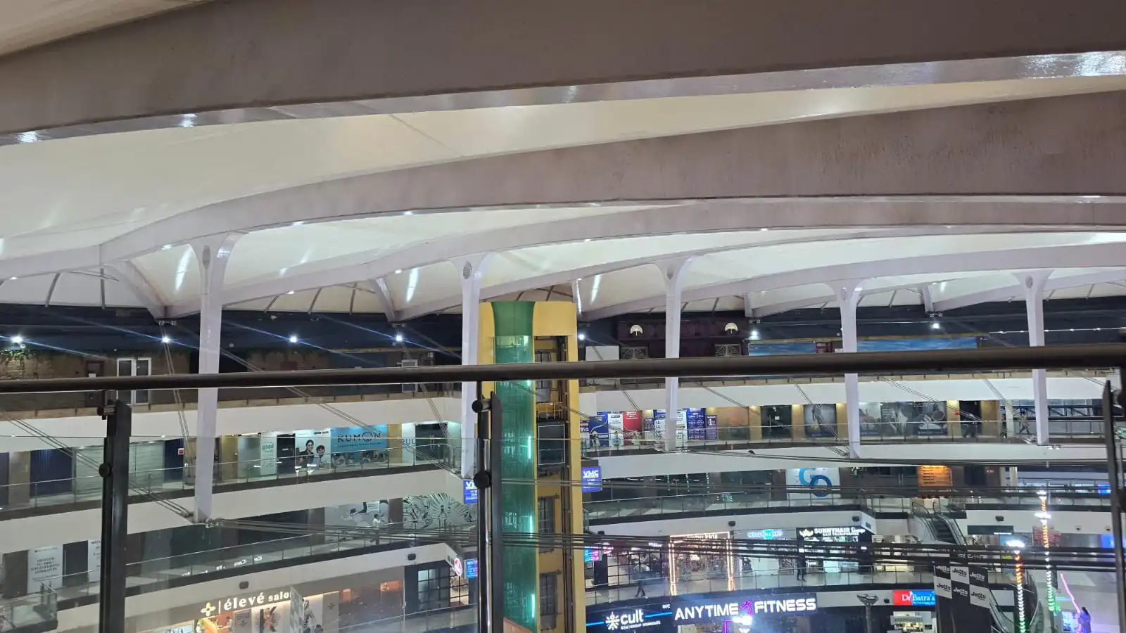 Vasant Square Mall Vasant Kunj — full-court view at dusk with the translucent membrane roof glowing over the lit retail frontages, Ekra Decor